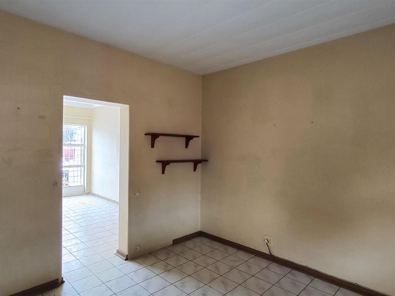 An empty room featuring tiled flooring and wall-mounted shelving, with a doorway leading to an adjacent tiled space.