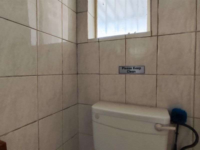 A compact bathroom featuring full-height wall tiling and a standard toilet suite with a small window for natural light.