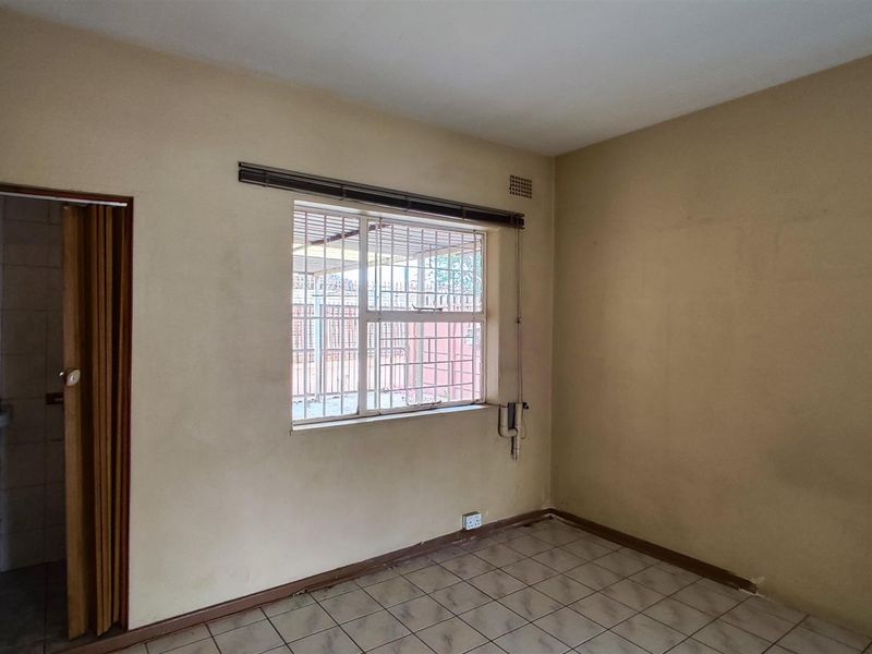 An empty bedroom featuring tiled flooring, a window with security bars, and an adjacent small bathroom with a basin.