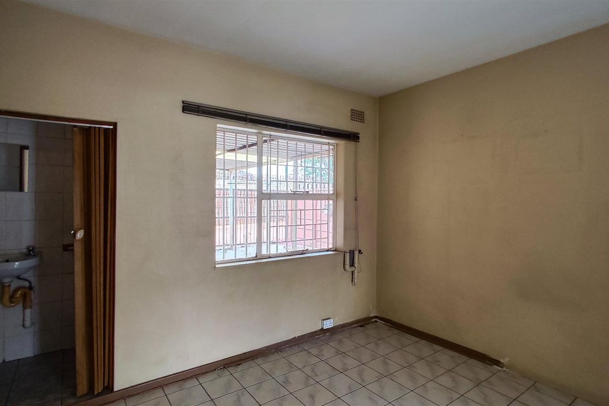 An empty bedroom featuring tiled flooring, a window with security bars, and an adjacent small bathroom with a basin.