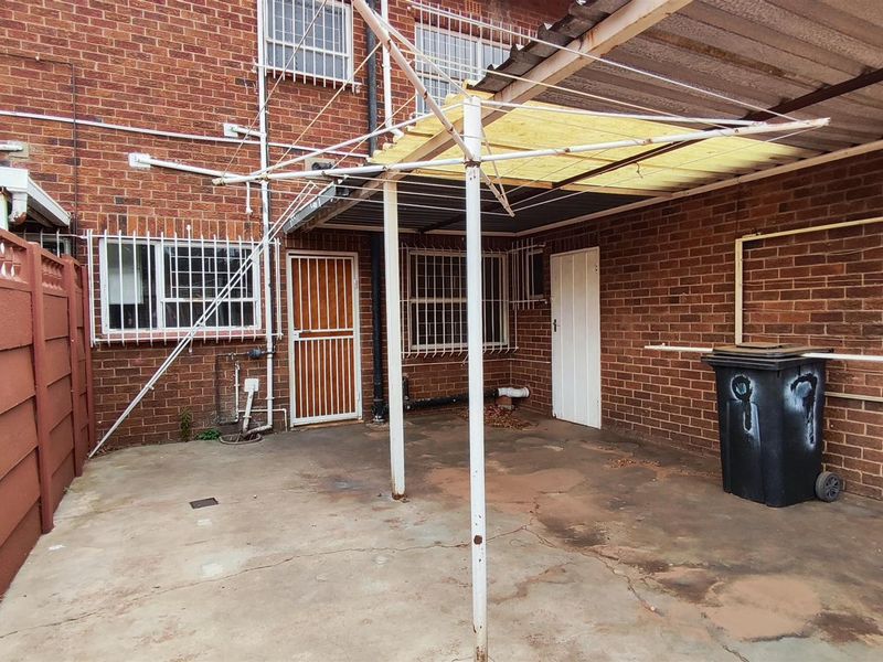 A rear courtyard area featuring a concrete patio, a covered outdoor structure, and brick wall finishes with security bars on windows and doors.