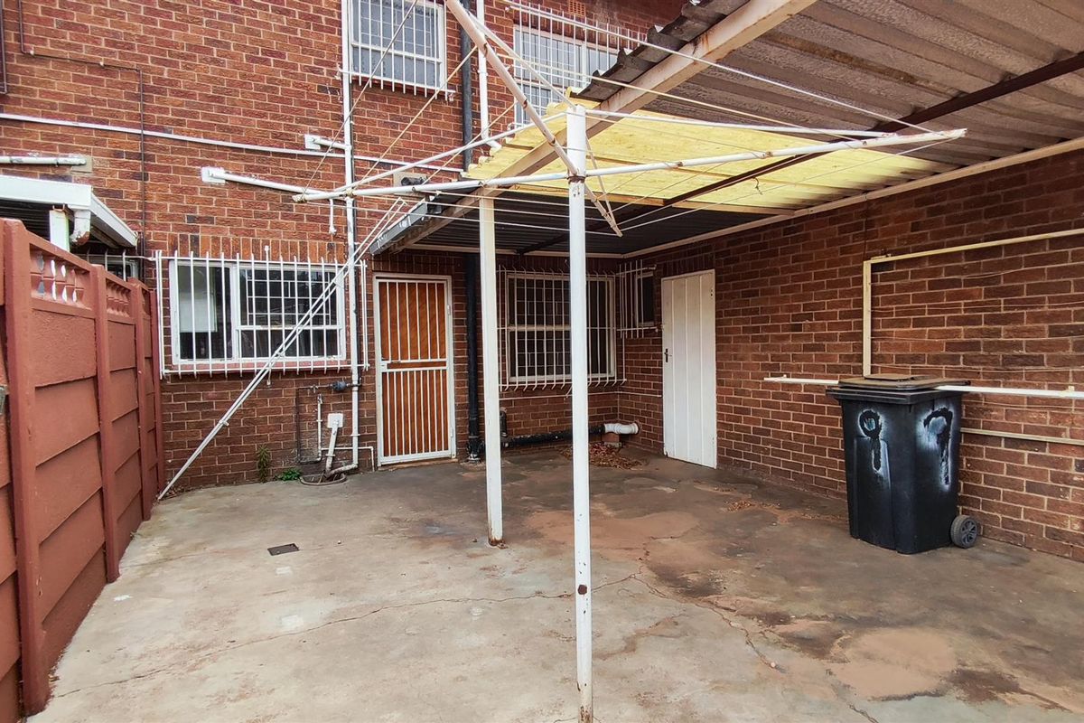 A rear courtyard area featuring a concrete patio, a covered outdoor structure, and brick wall finishes with security bars on windows and doors.