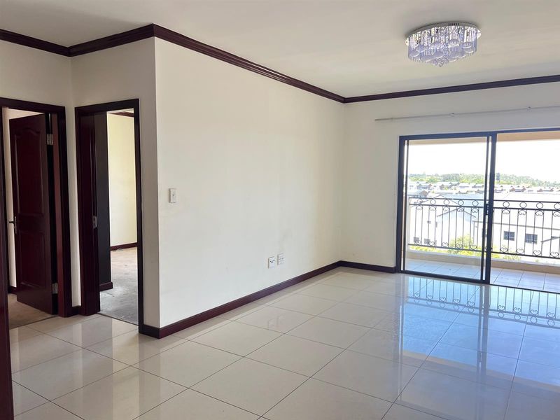A bright, empty living room featuring polished tile floors, dark wood trim, a decorative chandelier, and sliding doors leading to a balcony.