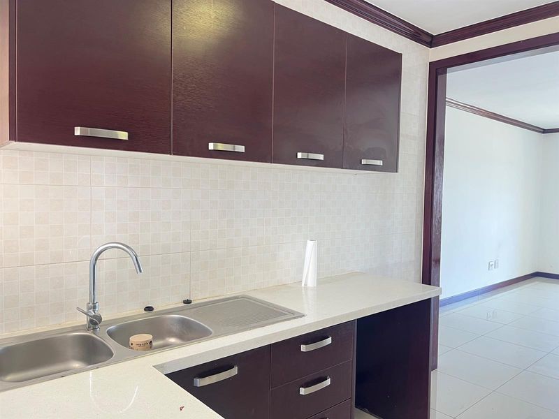 A clean, functional kitchen featuring dark wood cabinetry, stone countertops, a stainless steel double sink, and a neutral tiled backsplash.