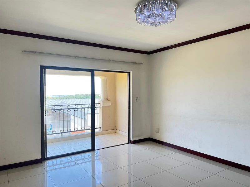 An empty living room featuring polished tile floors, crown molding, a decorative chandelier, and a sliding glass door leading to a private balcony.