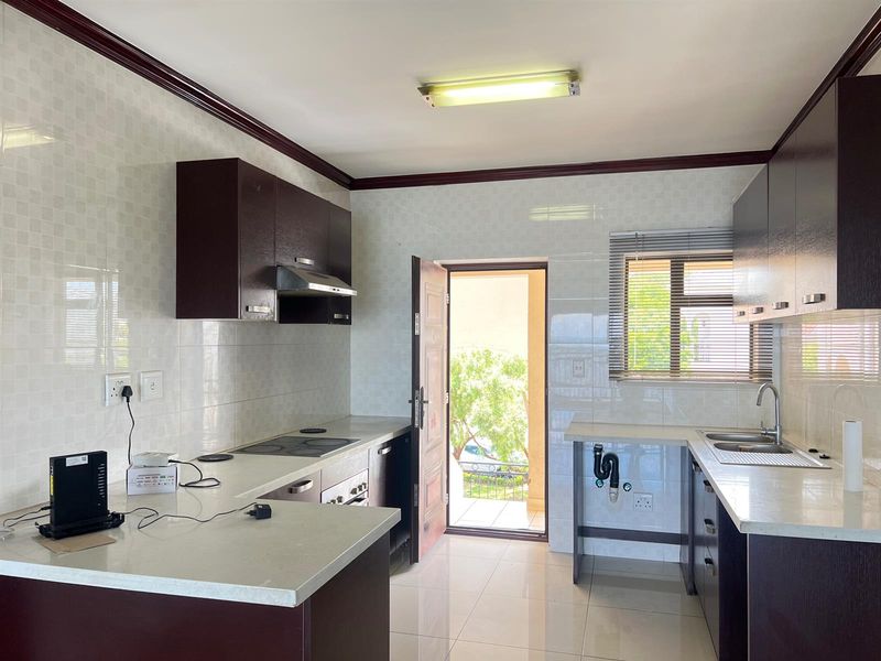 A functional kitchen featuring dark cabinetry, stone countertops, an electric hob, and direct access to an outdoor area.