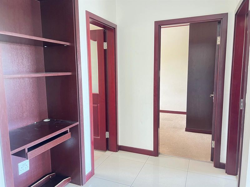 A hallway featuring built-in timber shelving, tiled flooring, and access to adjacent rooms through timber door frames.