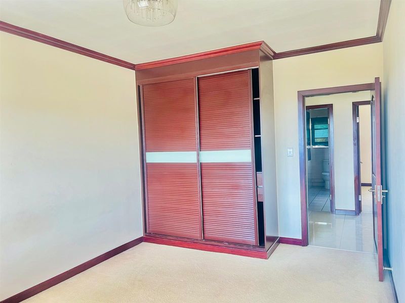 A bedroom featuring a built-in wooden wardrobe, crown molding, and carpet flooring, with an adjacent doorway leading to a bathroom.