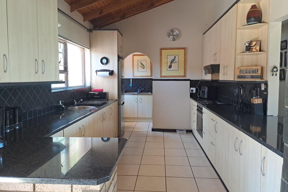 Spacious kitchen featuring light wood-tone cabinetry, dark granite countertops, tiled backsplash, and a vaulted timber-beamed ceiling, with an adjoining scullery area.