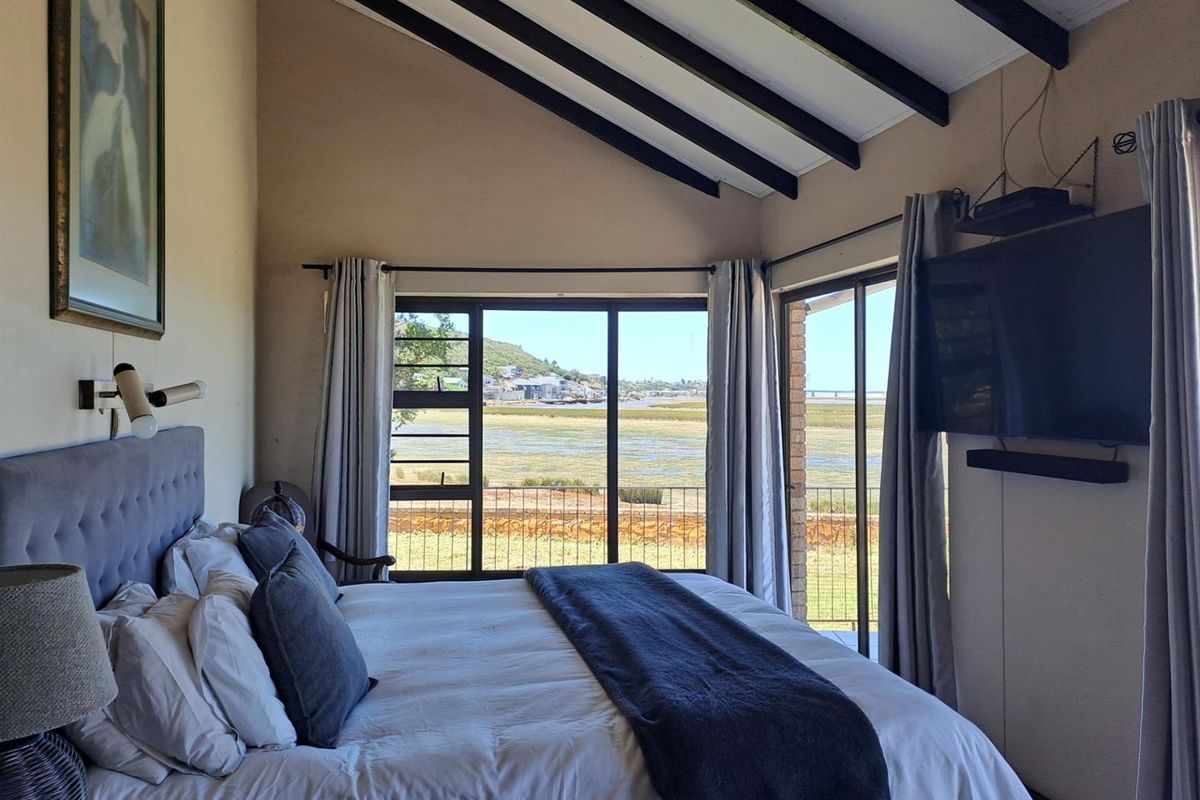 A bright bedroom featuring high vaulted ceilings with exposed beams, large windows, and sliding glass doors that offer expansive views of the surrounding landscape.