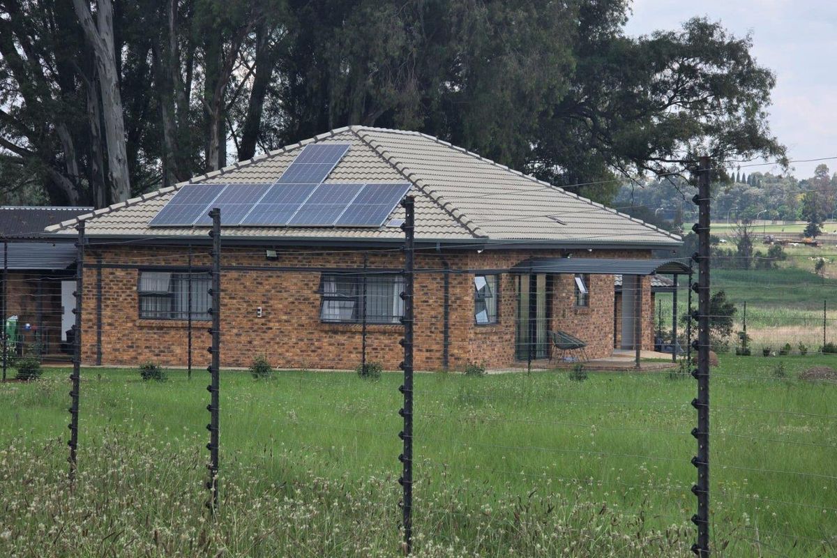 A face-brick farm dwelling featuring a tiled roof, integrated solar panel system, and secure perimeter electric fencing set within a rural landscape.