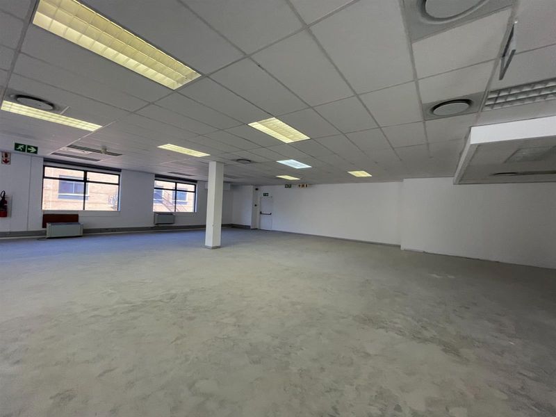 A spacious, open-plan office area featuring a suspended ceiling with recessed lighting, air conditioning vents, and an unfinished floor surface.
