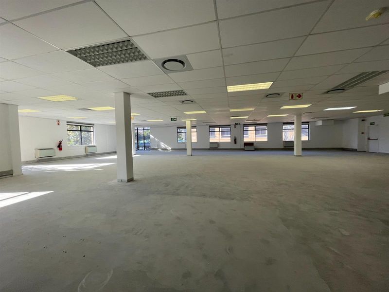 A spacious, open-plan office area featuring a suspended ceiling, recessed lighting, and large windows, currently awaiting final flooring installation.