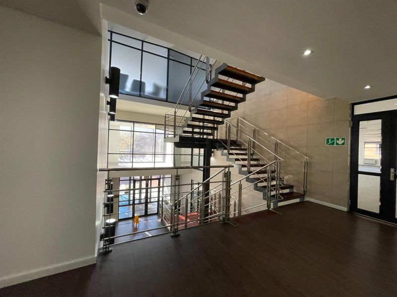 Modern office hallway featuring an open-tread staircase with stainless steel balustrades, glass partitions, and high-quality finishes throughout.