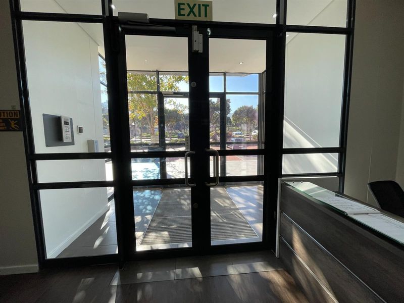 Modern office entrance featuring double glass doors with aluminum framing, a built-in reception desk, and an integrated intercom system.