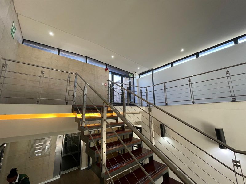Modern office building hallway featuring a contemporary staircase with stainless steel balustrades, recessed lighting, and elevator access.
