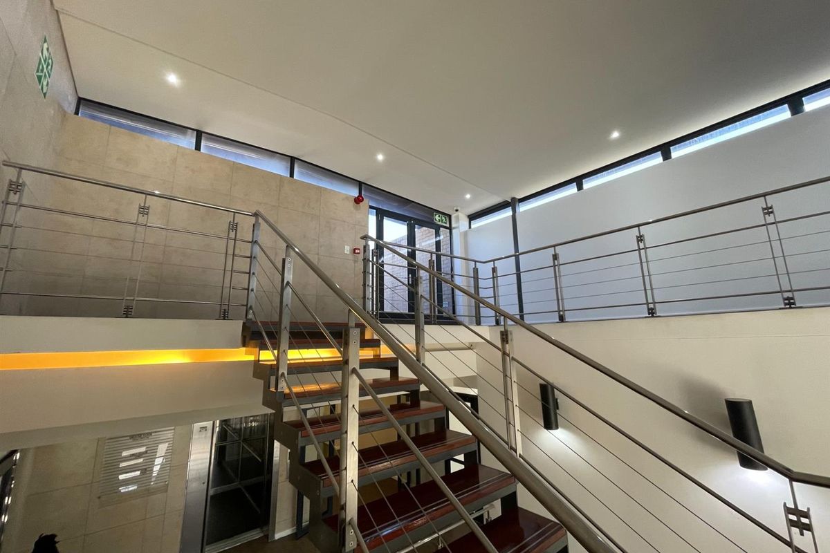 Modern office building hallway featuring a contemporary staircase with stainless steel balustrades, recessed lighting, and elevator access.
