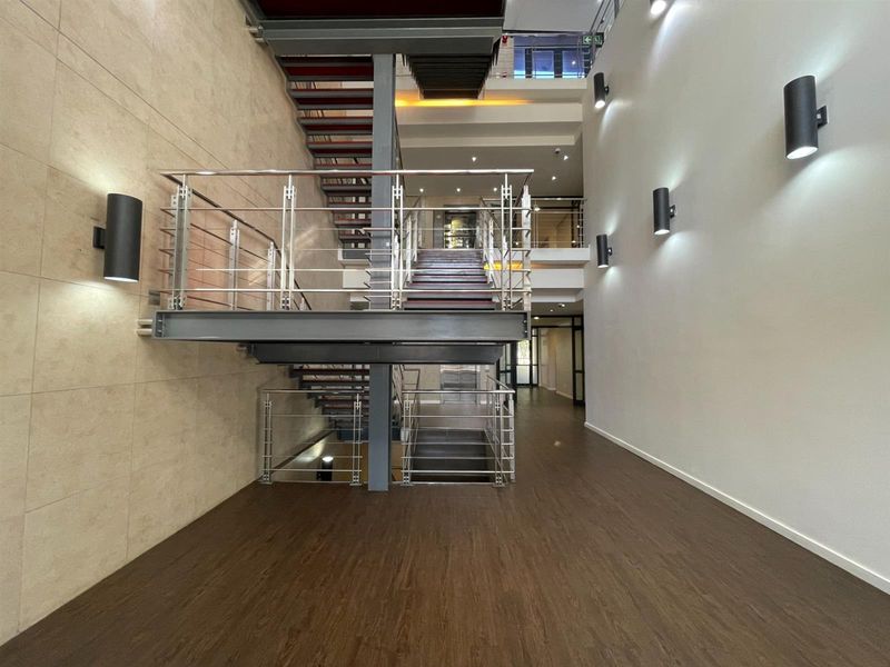 Modern office building entrance featuring a striking central steel staircase with stainless steel balustrades and contemporary wall-mounted lighting.