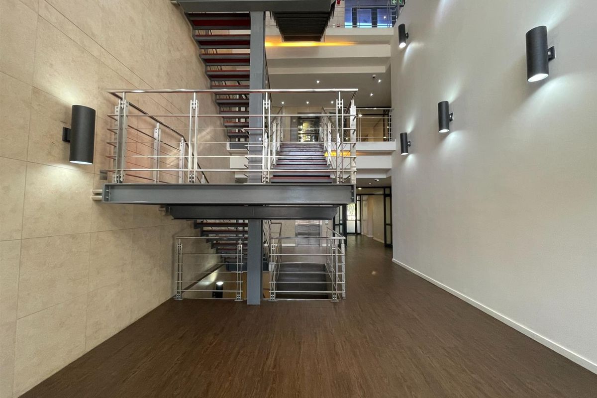 Modern office building entrance featuring a striking central steel staircase with stainless steel balustrades and contemporary wall-mounted lighting.