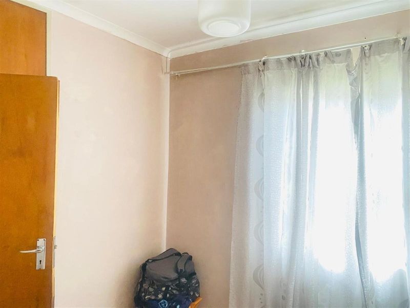 A simple bedroom featuring a built-in cupboard and a window with a curtain rail, requiring minor cosmetic updates to the wall finishes.