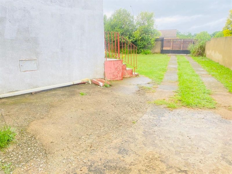 Rear exterior view showing a concrete driveway, metal staircase access, and a fenced garden area with boundary walls.