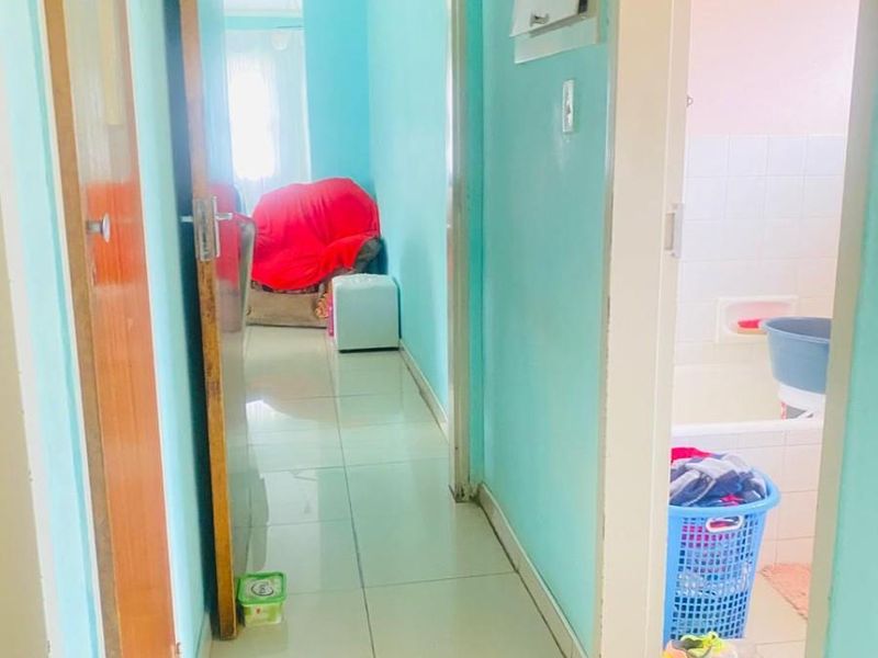 A narrow hallway with tiled flooring providing access to adjacent rooms, including a bathroom and living area.