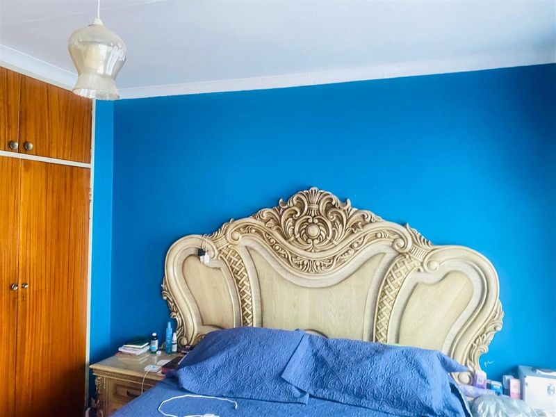 A bedroom featuring a built-in wooden wardrobe and decorative coving, finished with a bold blue accent wall.