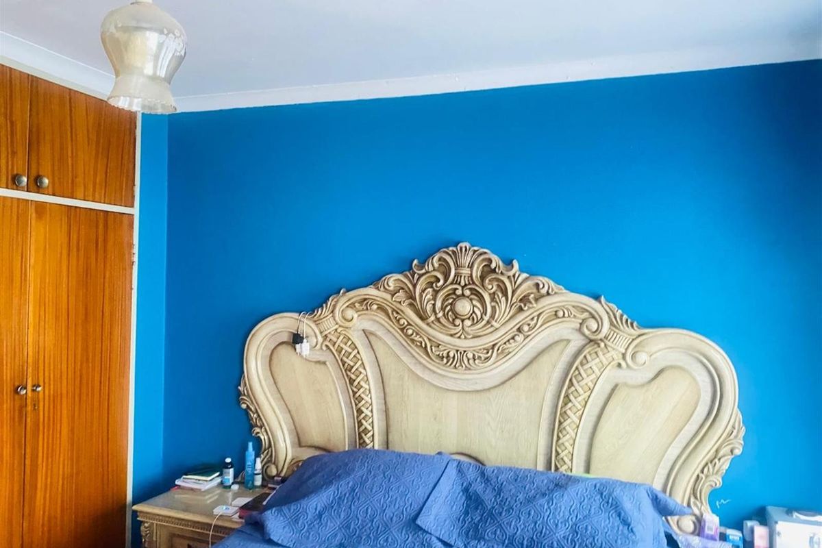 A bedroom featuring a built-in wooden wardrobe and decorative coving, finished with a bold blue accent wall.