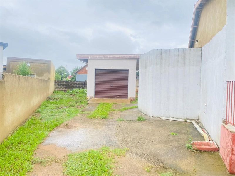 Rear exterior view featuring a detached garage with a roller door, concrete driveway, and surrounding boundary walls.