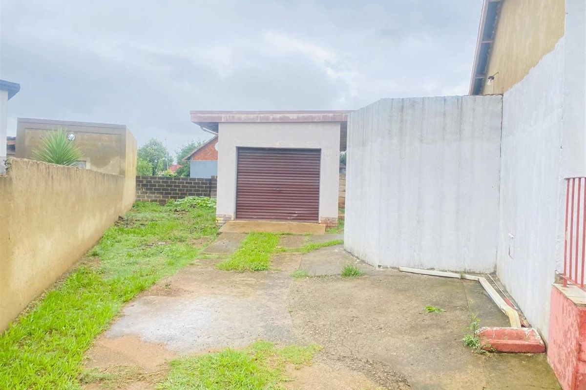 Rear exterior view featuring a detached garage with a roller door, concrete driveway, and surrounding boundary walls.