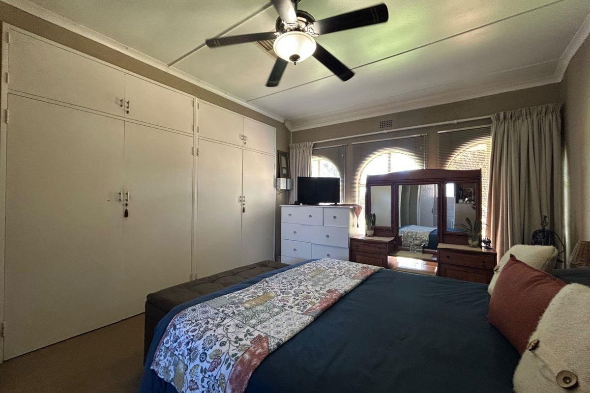 A bedroom featuring built-in floor-to-ceiling wardrobes, a ceiling fan, and distinctive arched windows with blinds.
