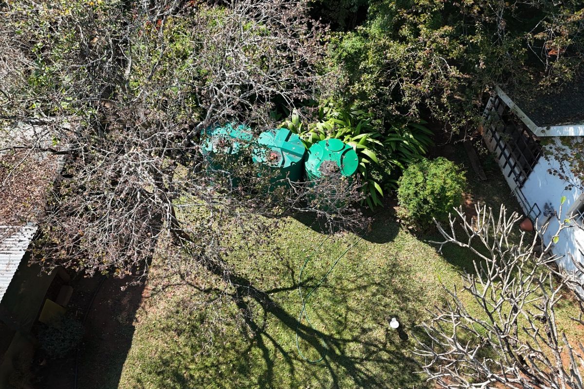 Aerial view of the property grounds featuring multiple water storage tanks situated within a garden area adjacent to the building structure.