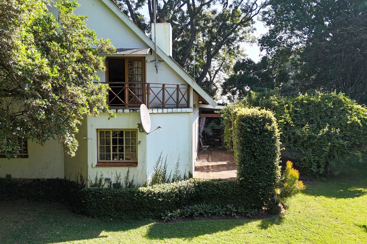 Rear view of the property featuring a covered patio, a first-floor balcony with timber railings, and established garden surroundings.
