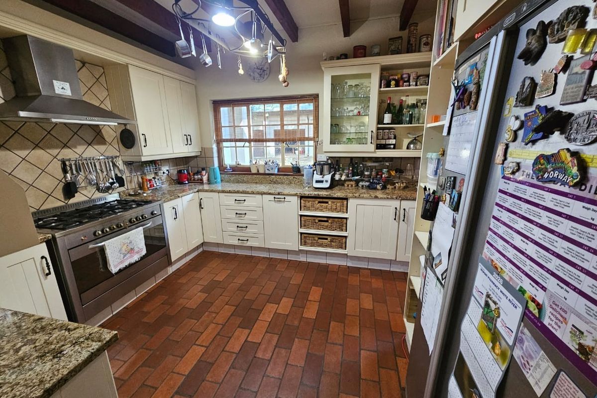 A rustic-style kitchen featuring granite countertops, built-in cabinetry, a gas stove with extractor fan, and terracotta tile flooring with exposed ceiling beams.