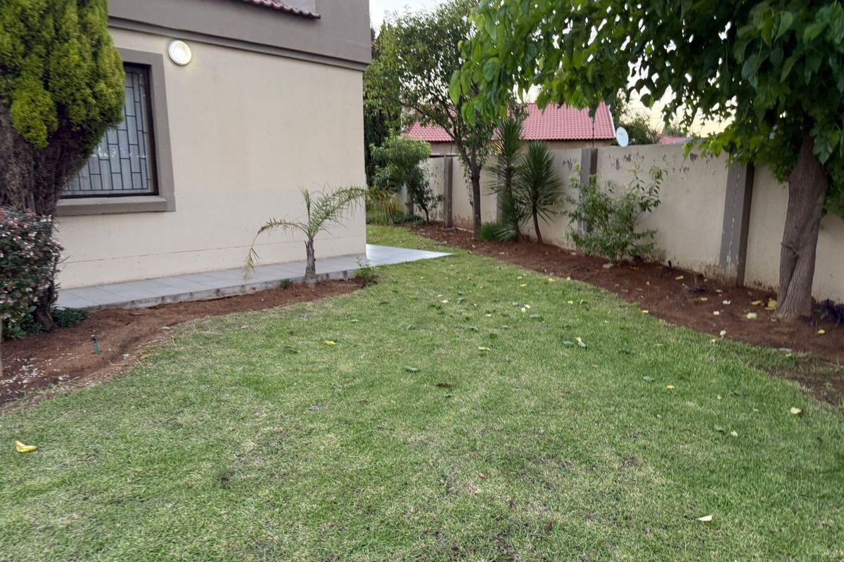 A private rear garden featuring a lawn area, perimeter boundary wall, and paved walkway adjacent to the house exterior.