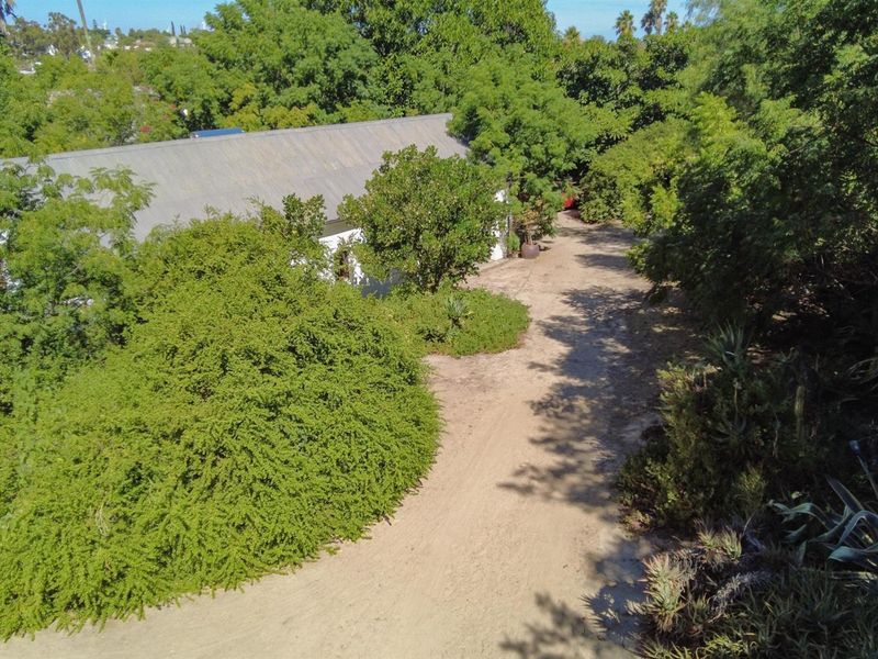 An aerial view of the property showing a large garden area with mature trees and a gravel driveway leading to the house.