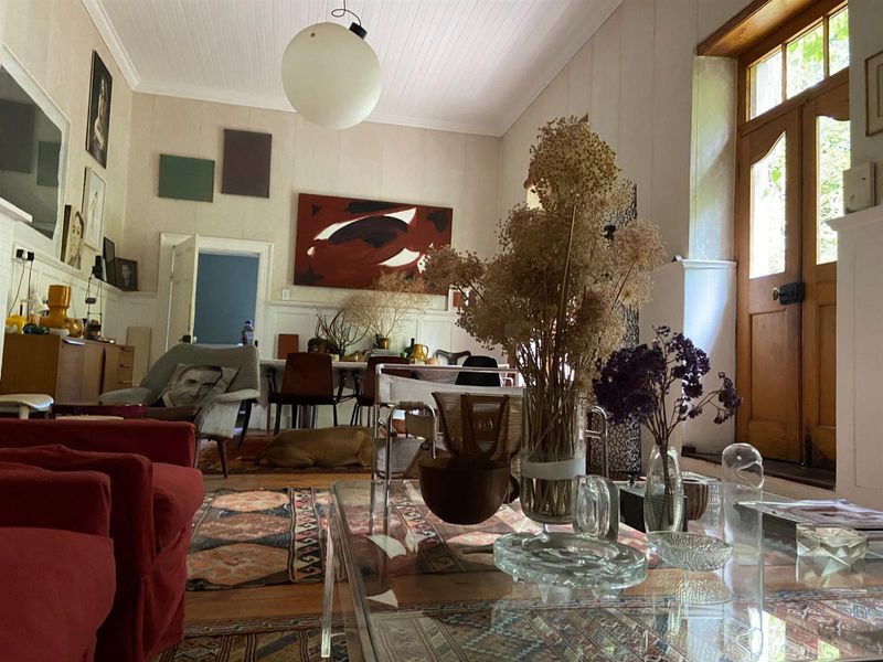 A spacious open-plan living and dining area featuring high ceilings, timber flooring, and a classic wooden entrance door with glass panels.