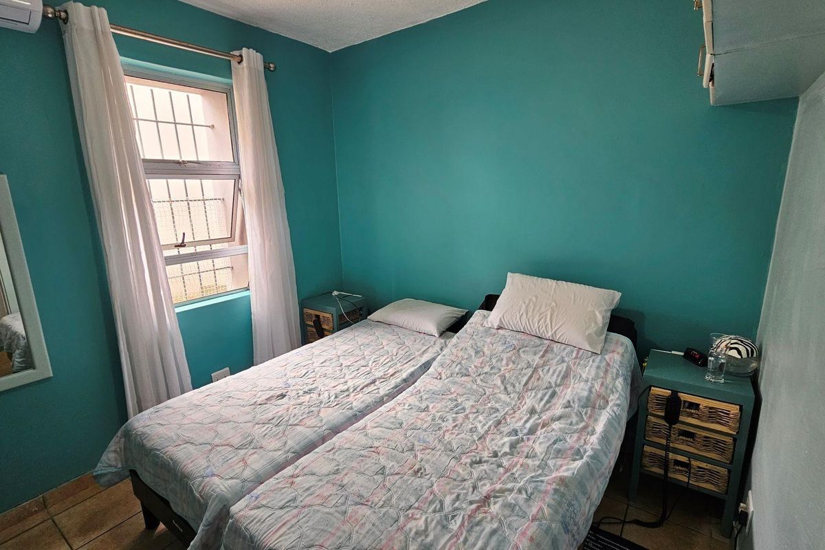 A bedroom featuring tiled flooring, a wall-mounted air conditioning unit, and a window with security bars.