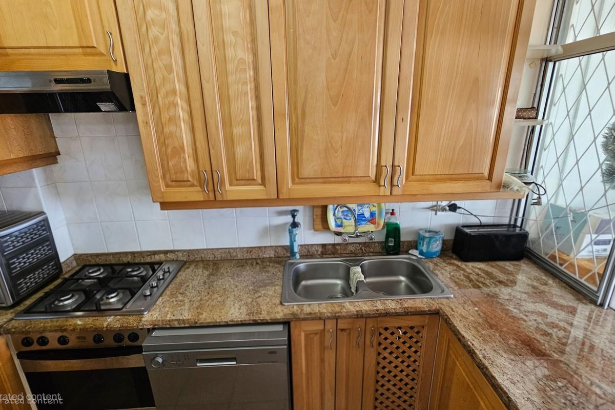 A functional kitchen featuring light wood cabinetry, granite countertops, a stainless steel gas hob, built-in oven, and a double basin sink.