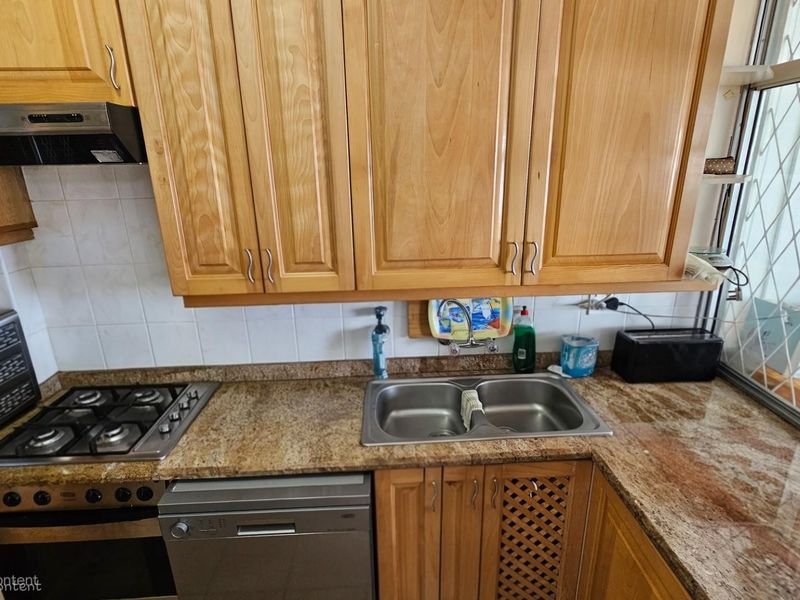 A functional kitchen featuring light wood cabinetry, granite countertops, a stainless steel gas hob, built-in oven, and a double basin sink.
