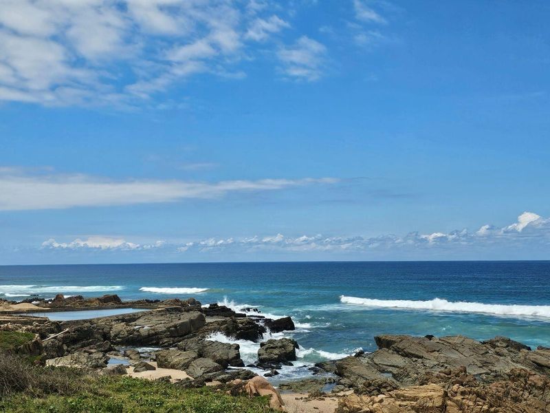 A scenic coastal view featuring rocky shoreline, ocean waves, and a natural tidal pool area.