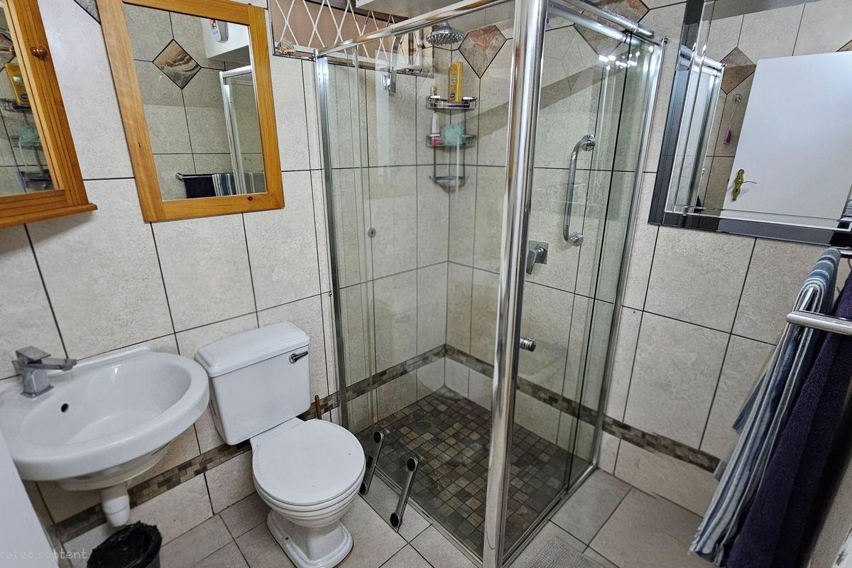 A functional bathroom featuring a glass-enclosed shower, pedestal basin, and toilet with neutral wall and floor tiling.