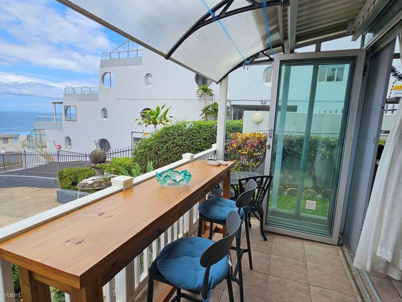 Covered balcony featuring tiled flooring, a built-in breakfast bar, and sliding glass doors, offering an outdoor seating area with coastal views.