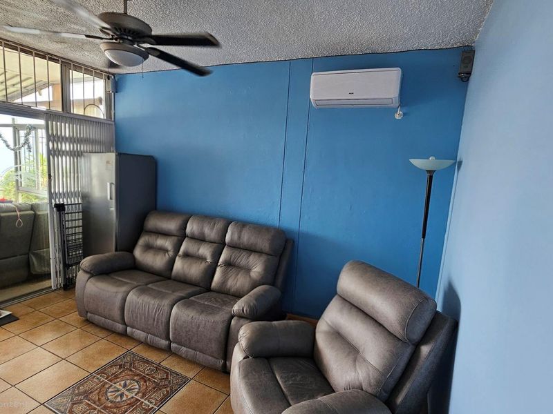 Living area featuring ceramic floor tiles, a ceiling fan, and a wall-mounted air conditioning unit with access to an enclosed patio.