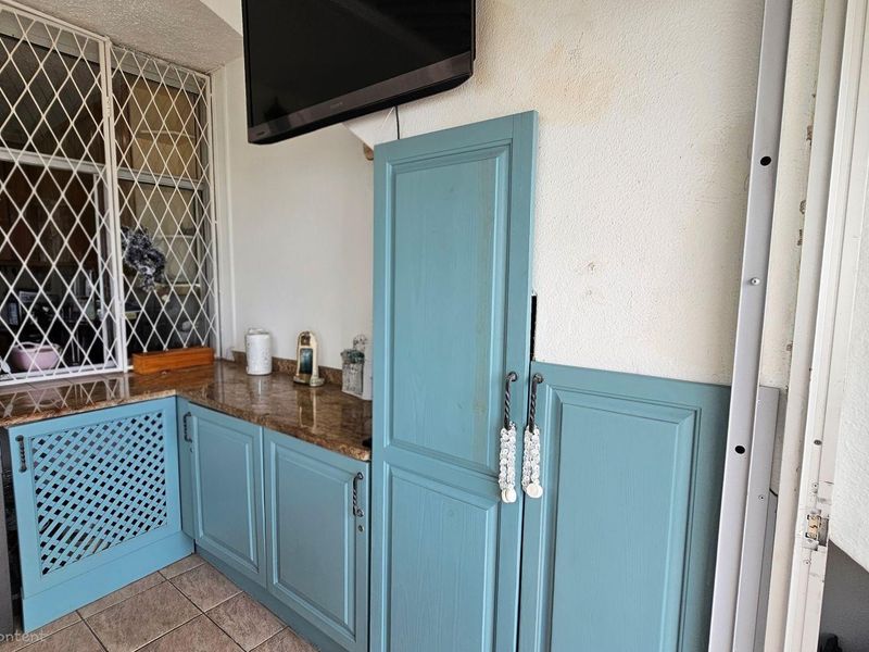 A laundry area featuring blue cabinetry, granite-style countertops, and a built-in washing machine, with security lattice on the window.