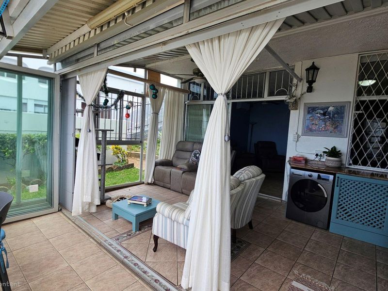 A covered patio area featuring tiled flooring, built-in cabinetry with integrated laundry appliance, and sliding glass doors leading to the garden.