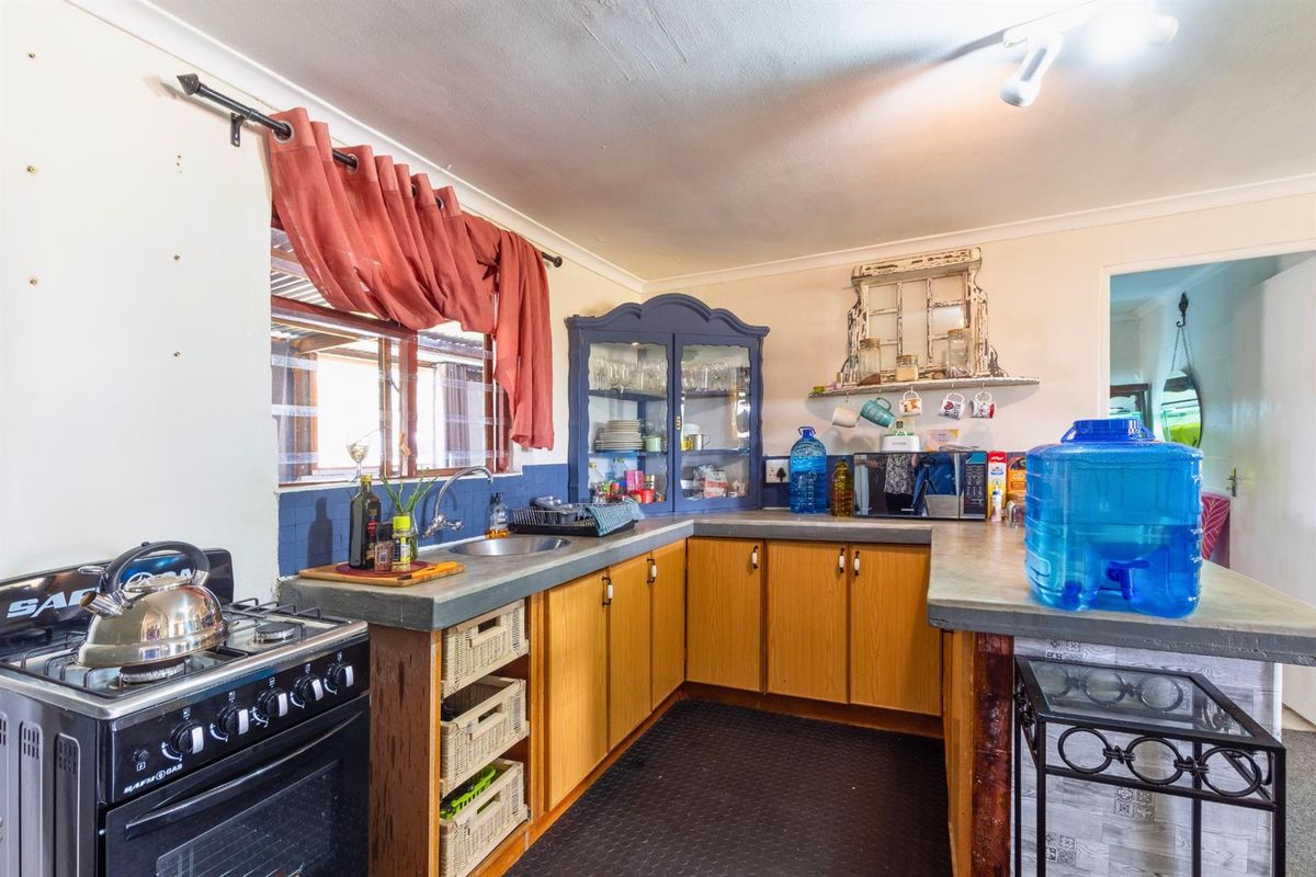 A functional kitchen featuring wooden cabinetry, concrete-style countertops, a gas stove, and a stainless steel sink with a tiled backsplash.