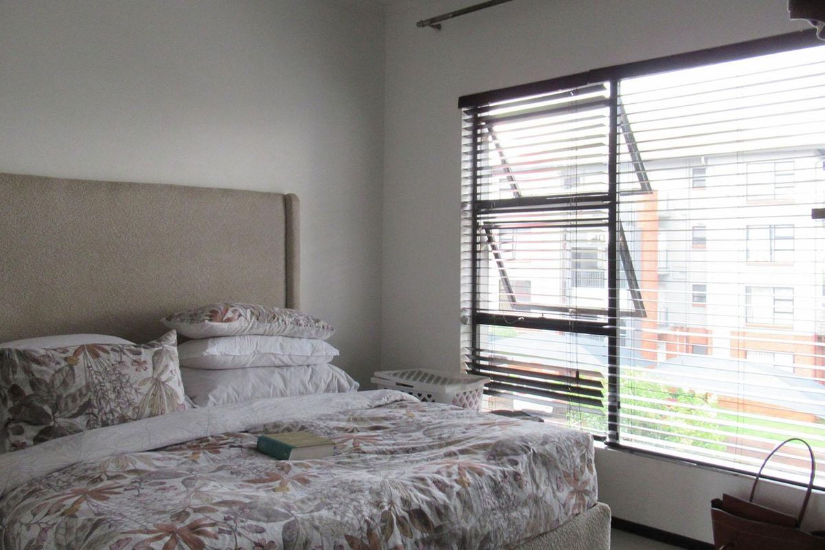 A bedroom featuring a large window with fitted horizontal blinds, providing natural light and an urban view.