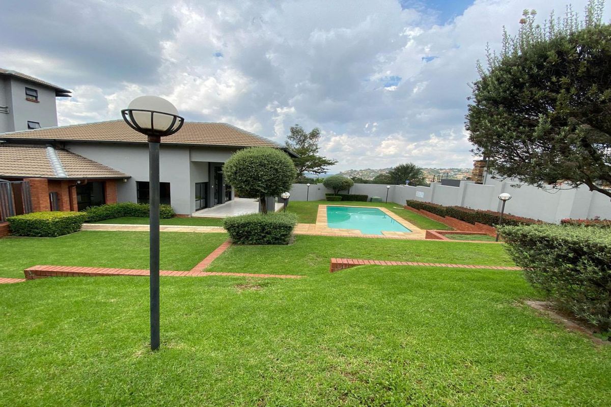 A well-maintained rear garden featuring a swimming pool, manicured lawn, brick pathways, and perimeter walling, offering a pleasant outdoor living space.