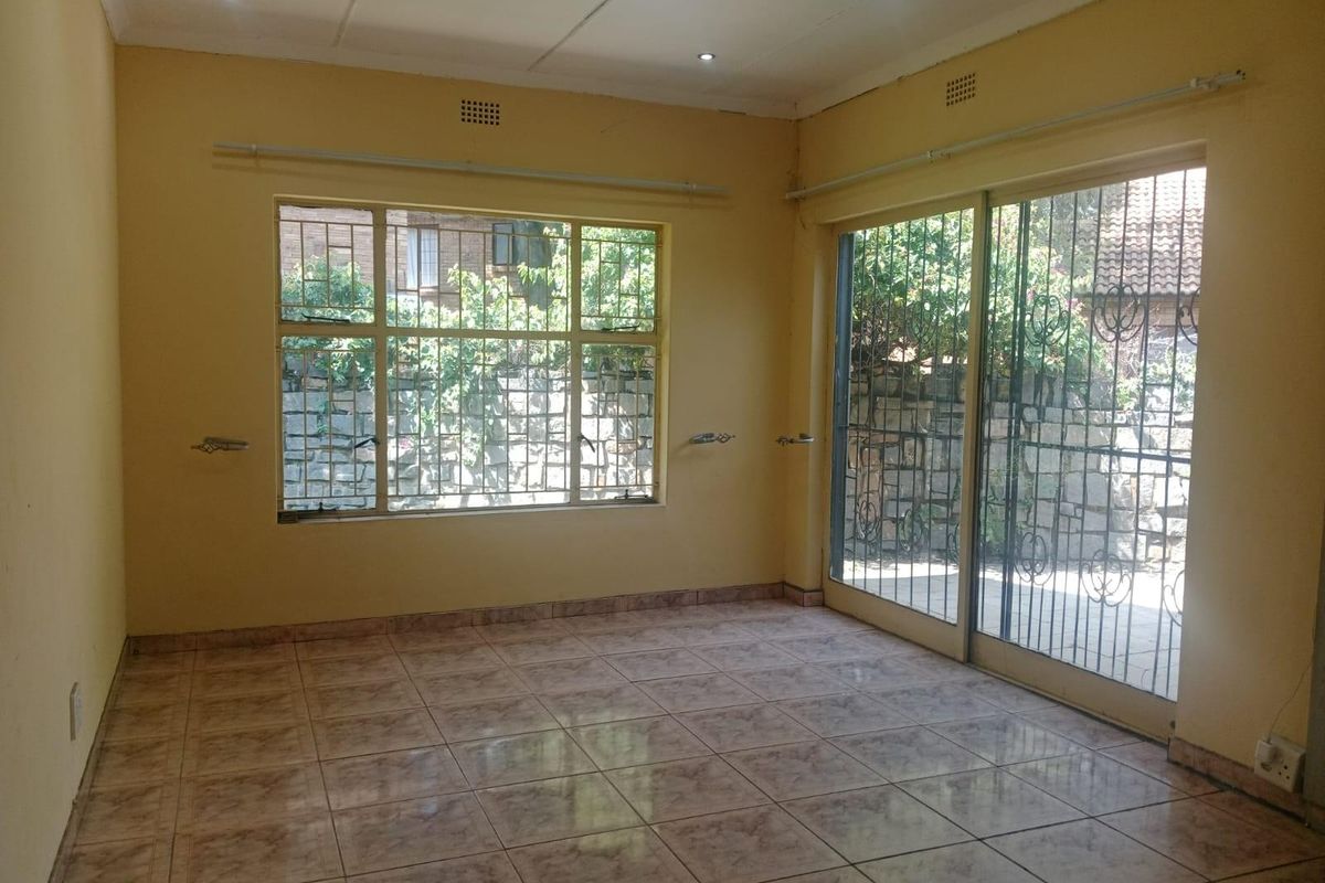 An empty living room featuring tiled flooring, recessed lighting, and large windows with security bars, offering a bright and functional space.